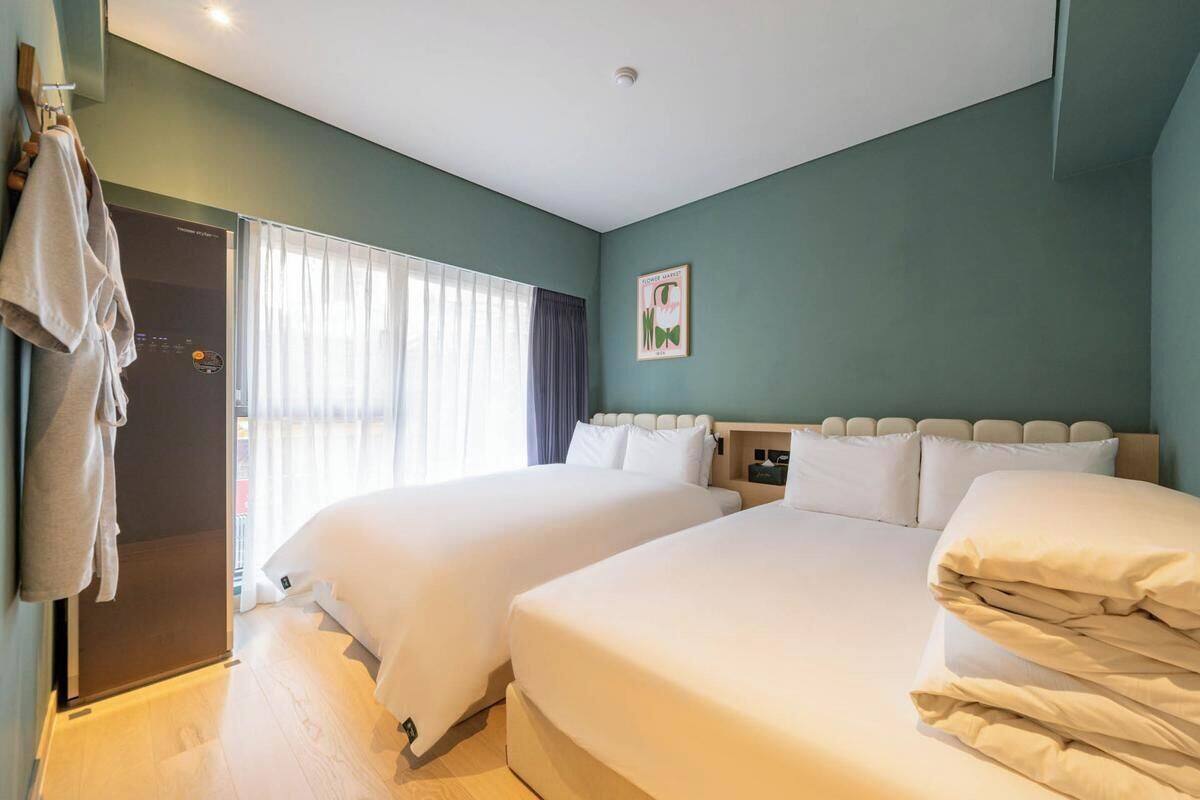 Ein Hotelzimmer mit zwei Betten, einer Dusche, einem Fenster mit Vorhängen und einem Handtuchhalter.