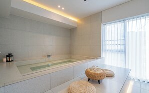 A modern bathroom with a large bathtub, a glass-enclosed shower, and a seating area with woven stools. - Brown-dot Hotel Haeundae (Busan)