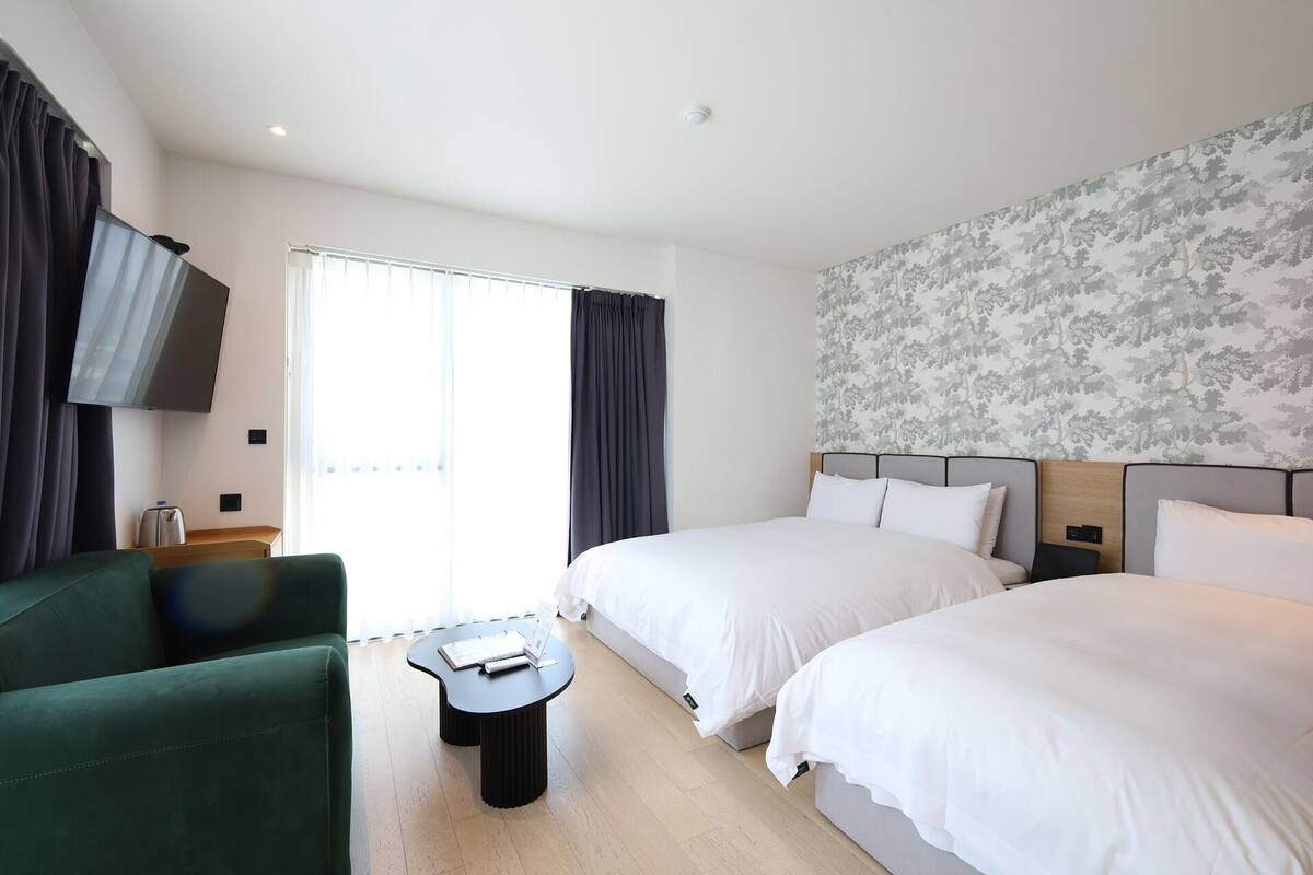 Ein Hotelzimmer mit zwei Betten, einem grünen Sofa, einem kleinen Tisch und einem Fernseher.