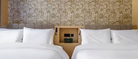Een hotelkamer met bloemenbehang, een houten hoofdbord en een inbouwkastje met een klein zwart voorwerp.
