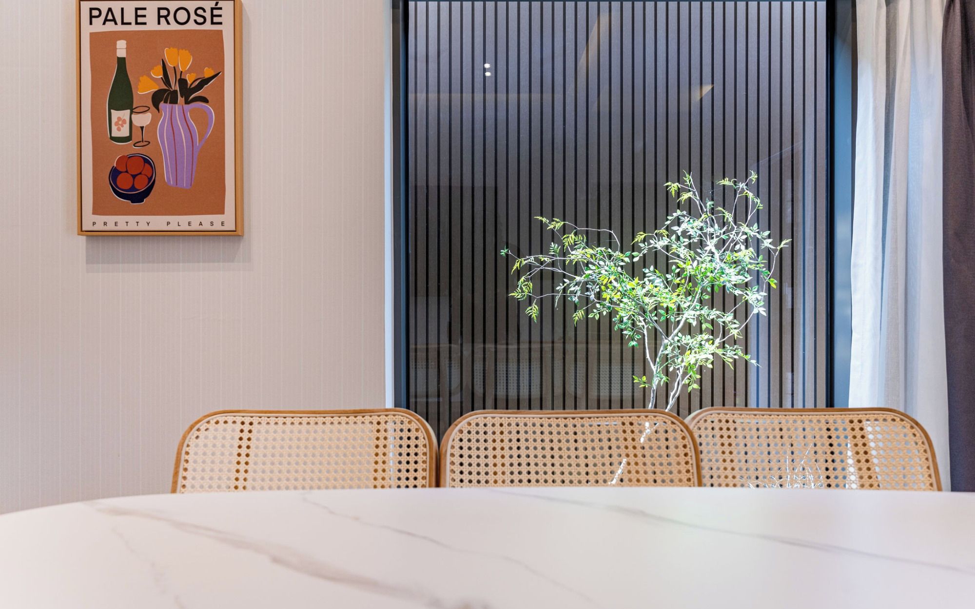 A dining area with a marble table, wicker chairs, a potted plant, and a poster on the wall.