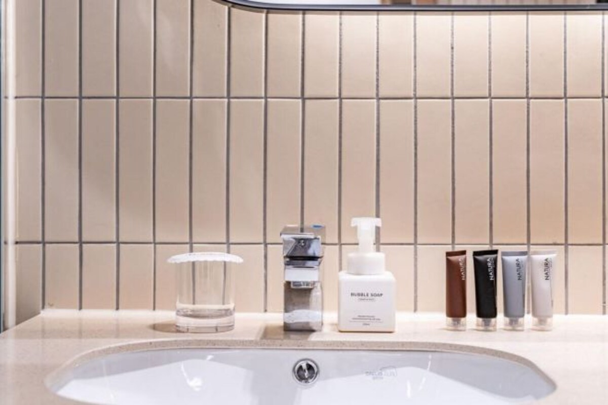 A bathroom with a sink, a faucet, a glass, and a row of toiletries.