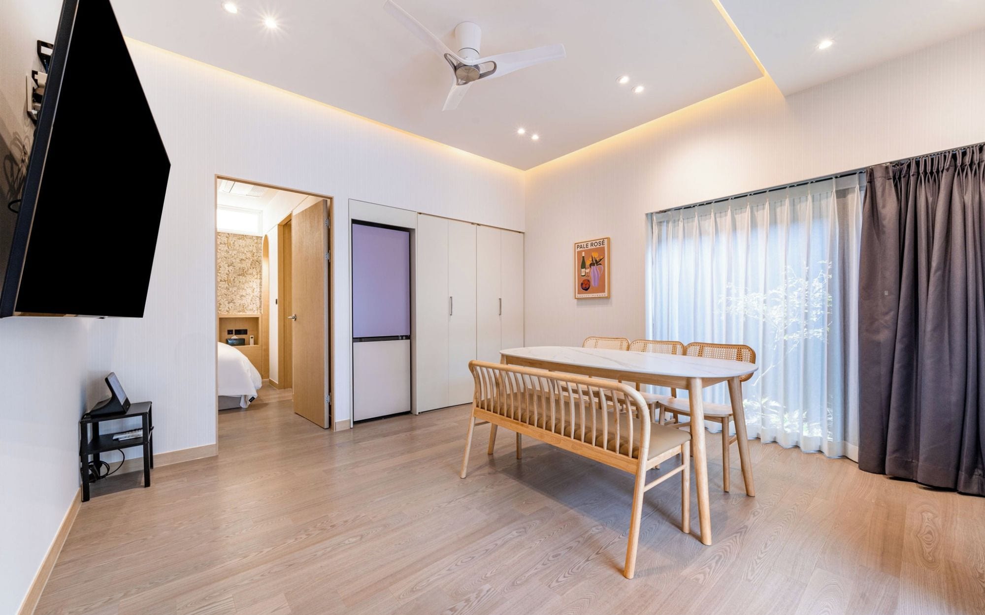 A modern living room with a dining table, a ceiling fan, and a view of a bedroom.