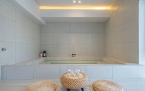 A modern bathroom with a large bathtub, two woven poufs, and a small lantern on the floor. - Brown-dot Hotel Haeundae (Busan)