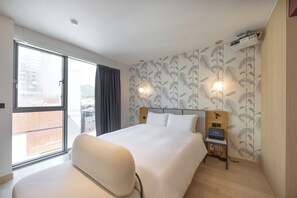 A hotel room with a large bed, a desk with a laptop, a projector, and a view of the city through a large window. - Brown-dot Hotel Haeundae (Busan)