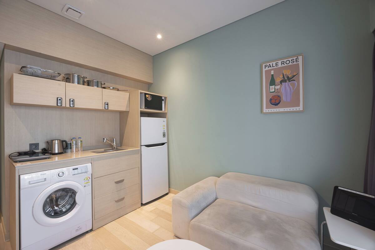 Eine kompakte Küche mit Waschmaschine, Kühlschrank und Essbereich inklusive Sofa und Tisch.