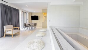 A modern living room with a sofa, dining table, and TV. There are three woven ottomans on the floor. - Brown-dot Hotel Haeundae (Busan)