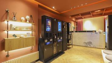 A hotel reception area with self-service card kiosks, a reception desk, and a wooden floor.