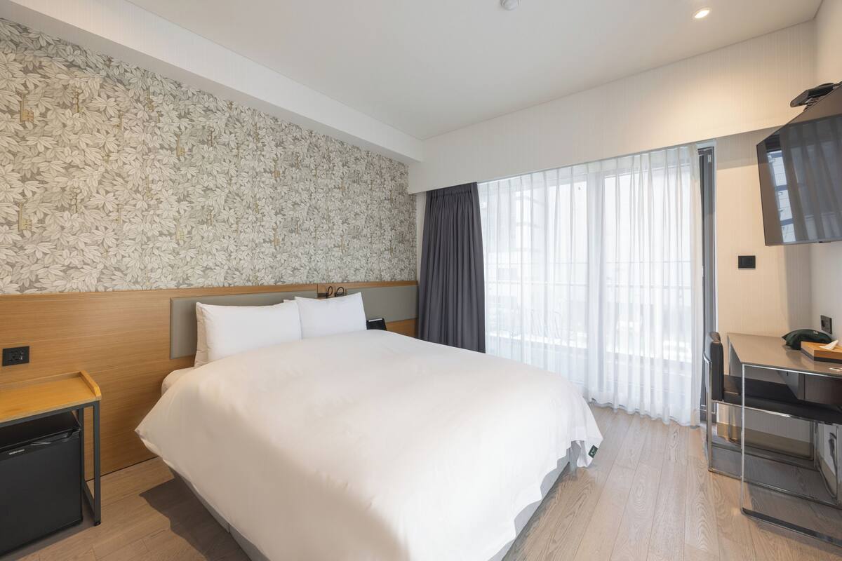Ein modernes Hotelzimmer mit einem großen Bett, einem Schreibtisch und einem Fenster mit Vorhängen.