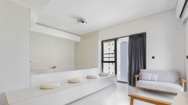A modern living room with a white sofa, a wooden bench, and a large window with curtains. - Brown-dot Hotel Haeundae (Busan)