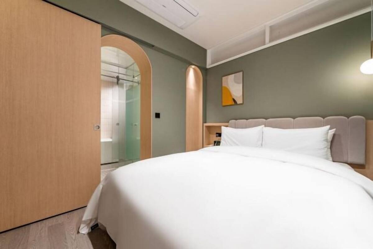 Ein modernes Hotelzimmer mit einem großen Bett, einem Holzschrank, einer Glasdusche und einem schlichten Wanddesign.
