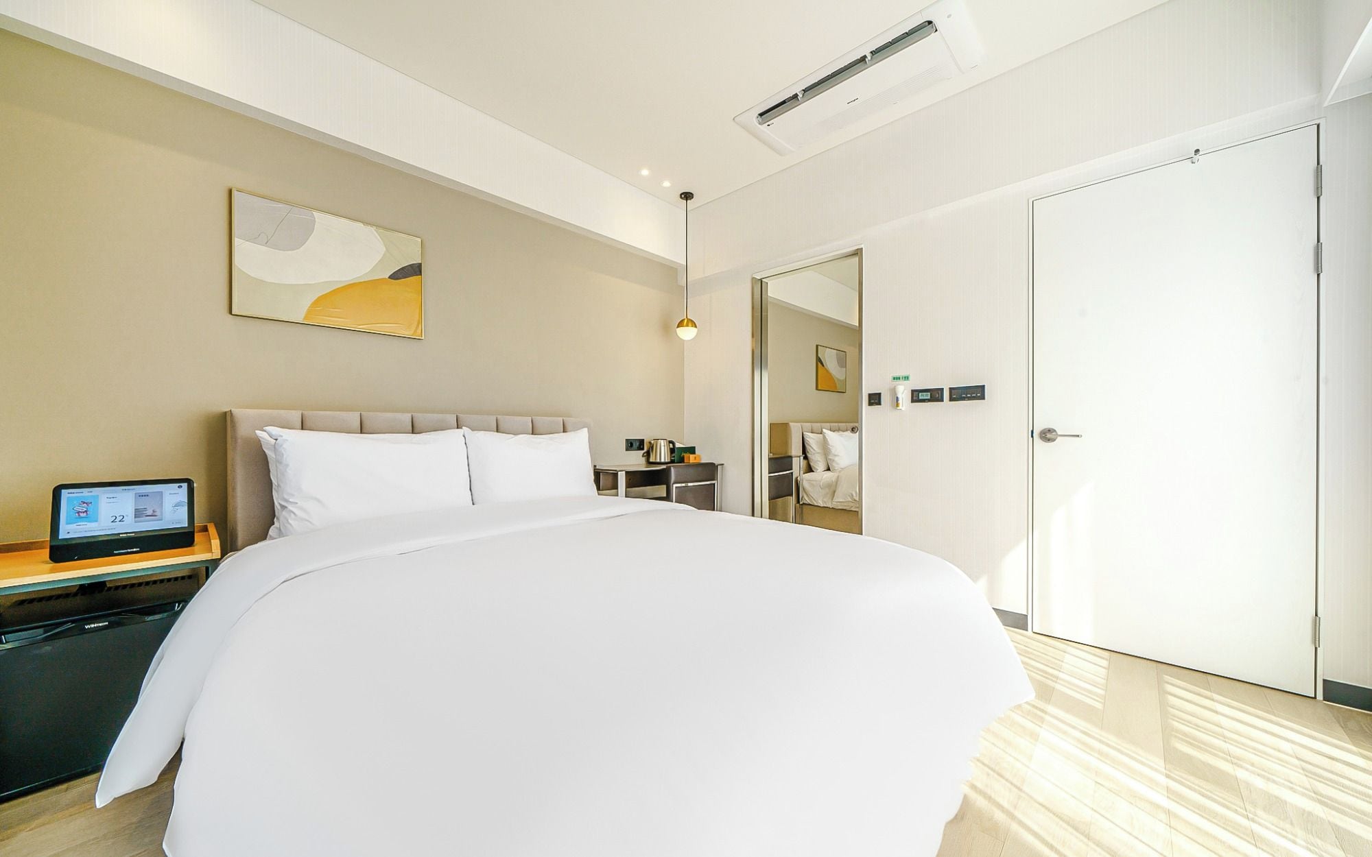 Ett hotellrum med en stor säng, ett nattduksbord med en digital enhet, ett litet bord med en vattenkokare och en garderob.