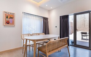 A dining area with a round table and wooden chairs, a bench, and a view through a glass door to an outdoor patio. - Brown-dot Hotel Haeundae (Busan)