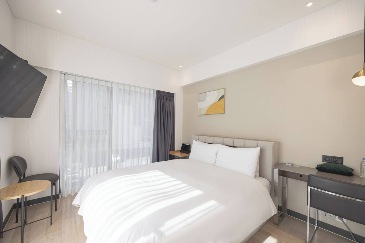 Ein Hotelzimmer mit einem großen Bett, einem Schreibtisch, einem Sessel und einem an der Wand befestigten Fernseher.