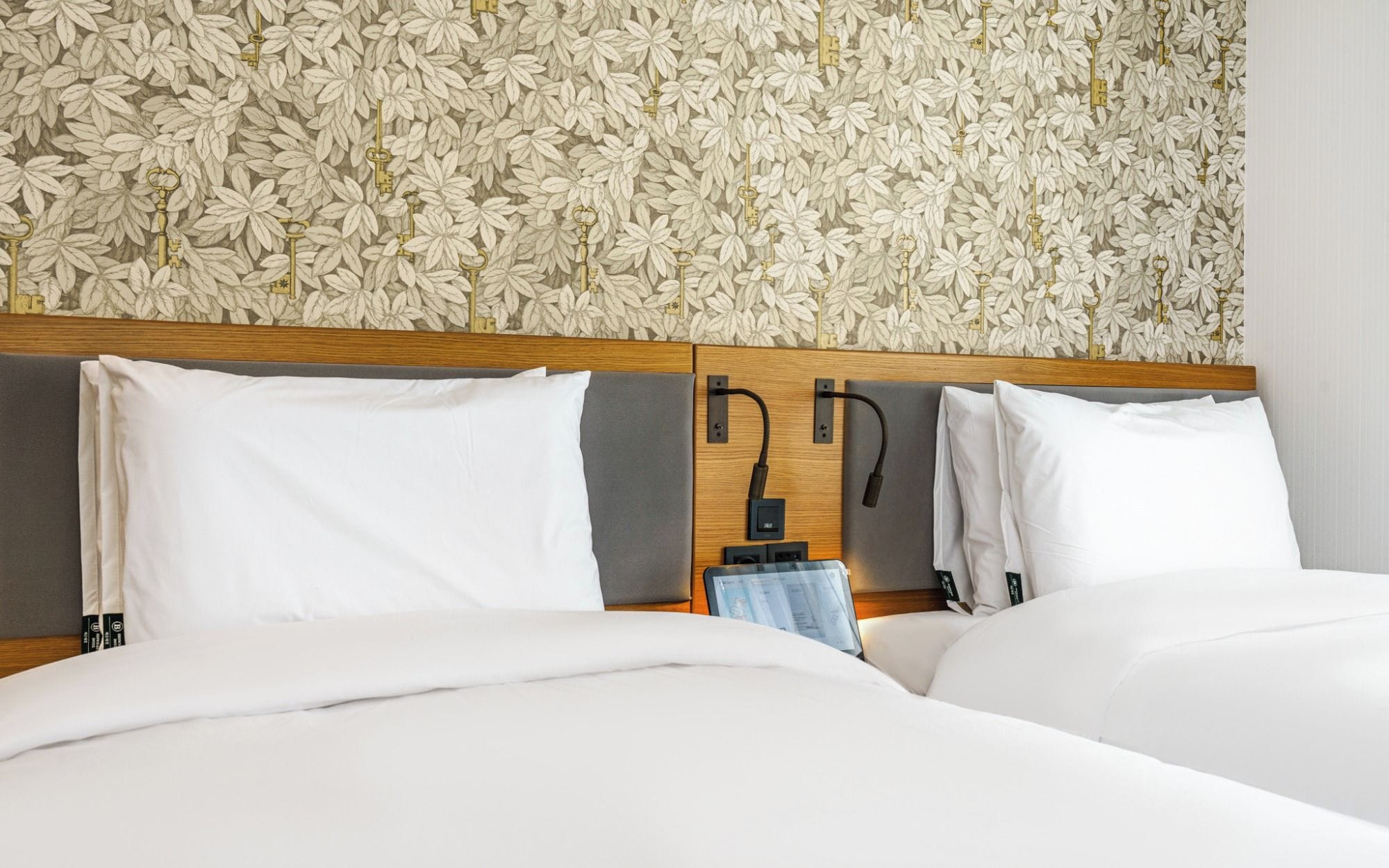 A hotel room with a bed, pillows, and a headboard with a floral wallpaper design.