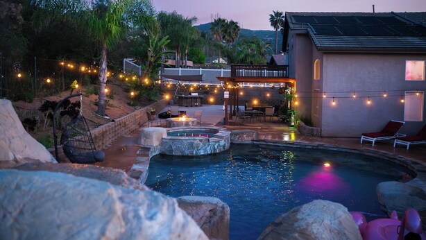 Un área de piscina con jacuzzi, sillones de descanso e iluminación colgante.