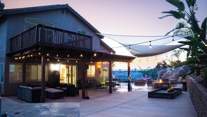 Un patio techado al aire libre con asientos, luces colgantes y vista a una zona de piscina.