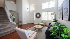 Amplia sala de estar con escalera, una mesa de centro redonda de madera, un sofá y una planta verde grande.