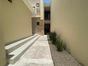 A narrow pathway leading to a building entrance with steps and a gravel area with plants. - Hotel 28 (Cancun)
