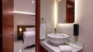 A hotel room with a large oval sink, a bedside table with a lamp, a wooden headboard, and a mirror with a wooden frame. - Hotel 28 (Cancun)