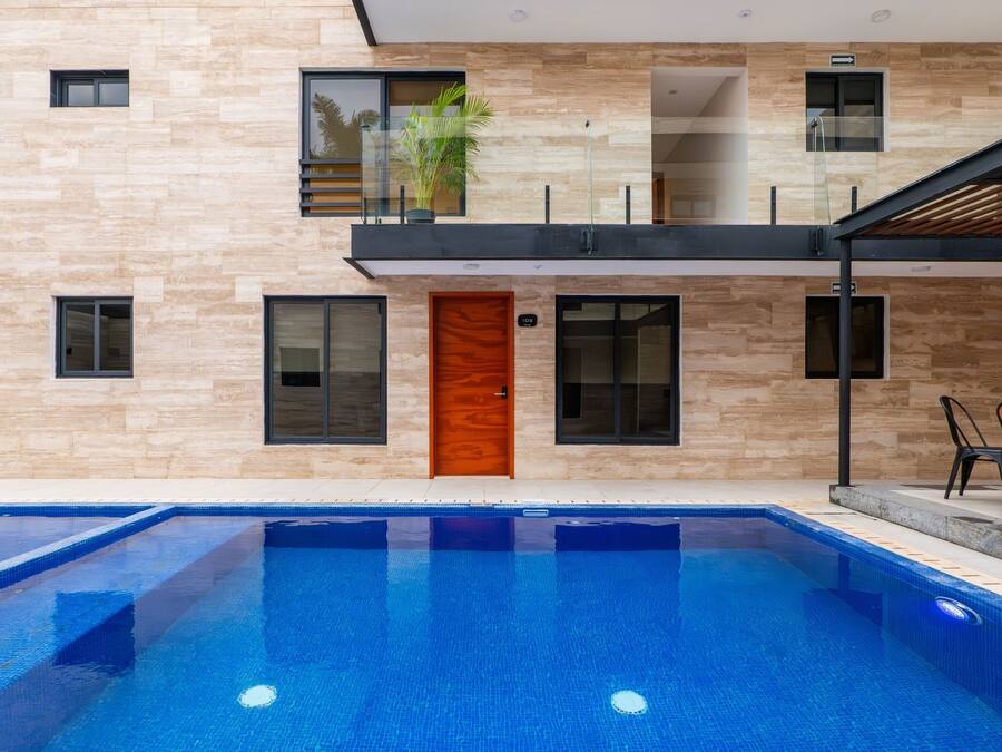 Ein modernes Gebäude mit Schwimmbad, einer Holztür und einem Balkon mit Pflanzen.