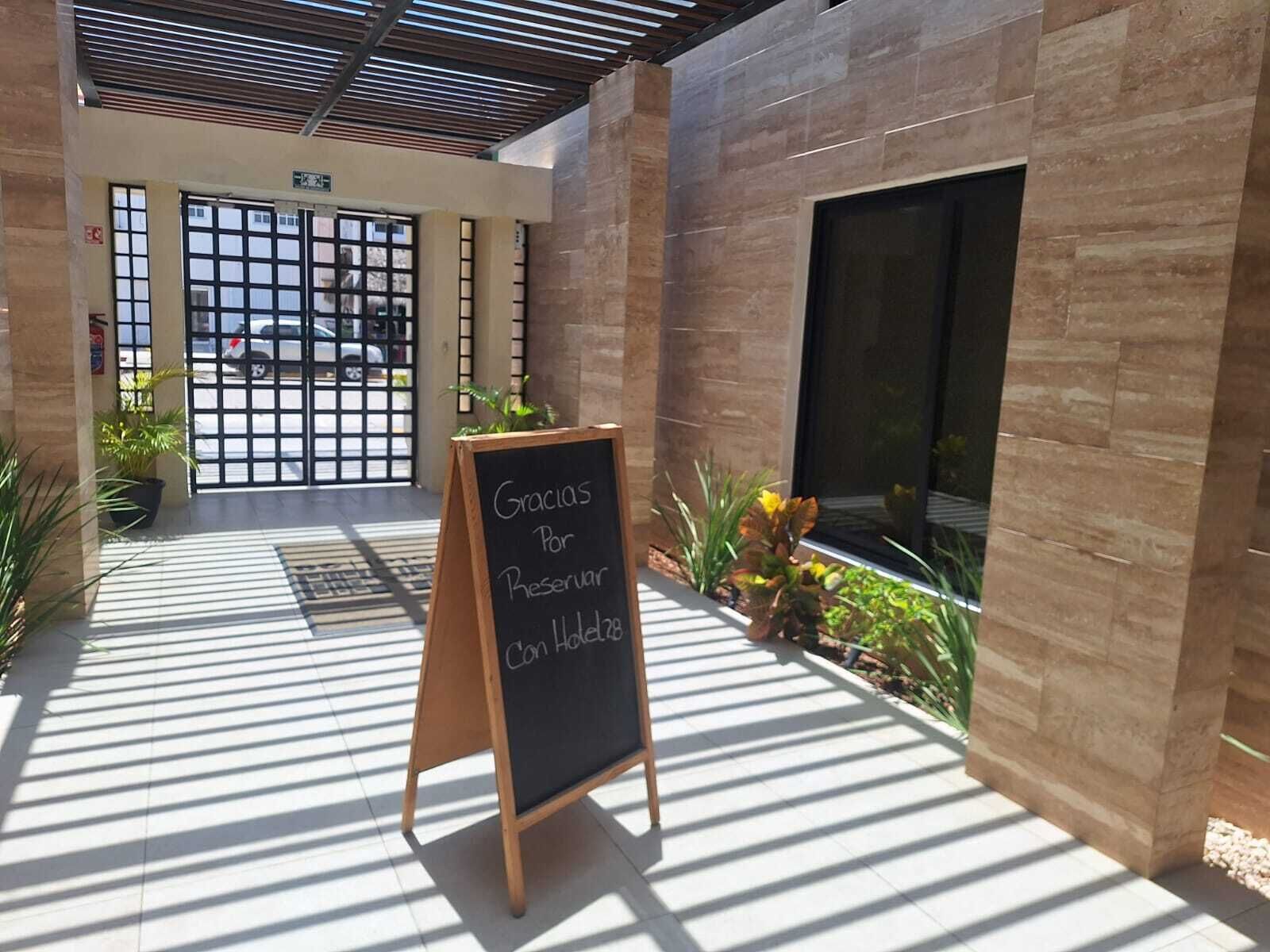 Entrada moderna de un edificio con un cartel en una pizarra, un camino de acceso con portones y plantas en macetas.
