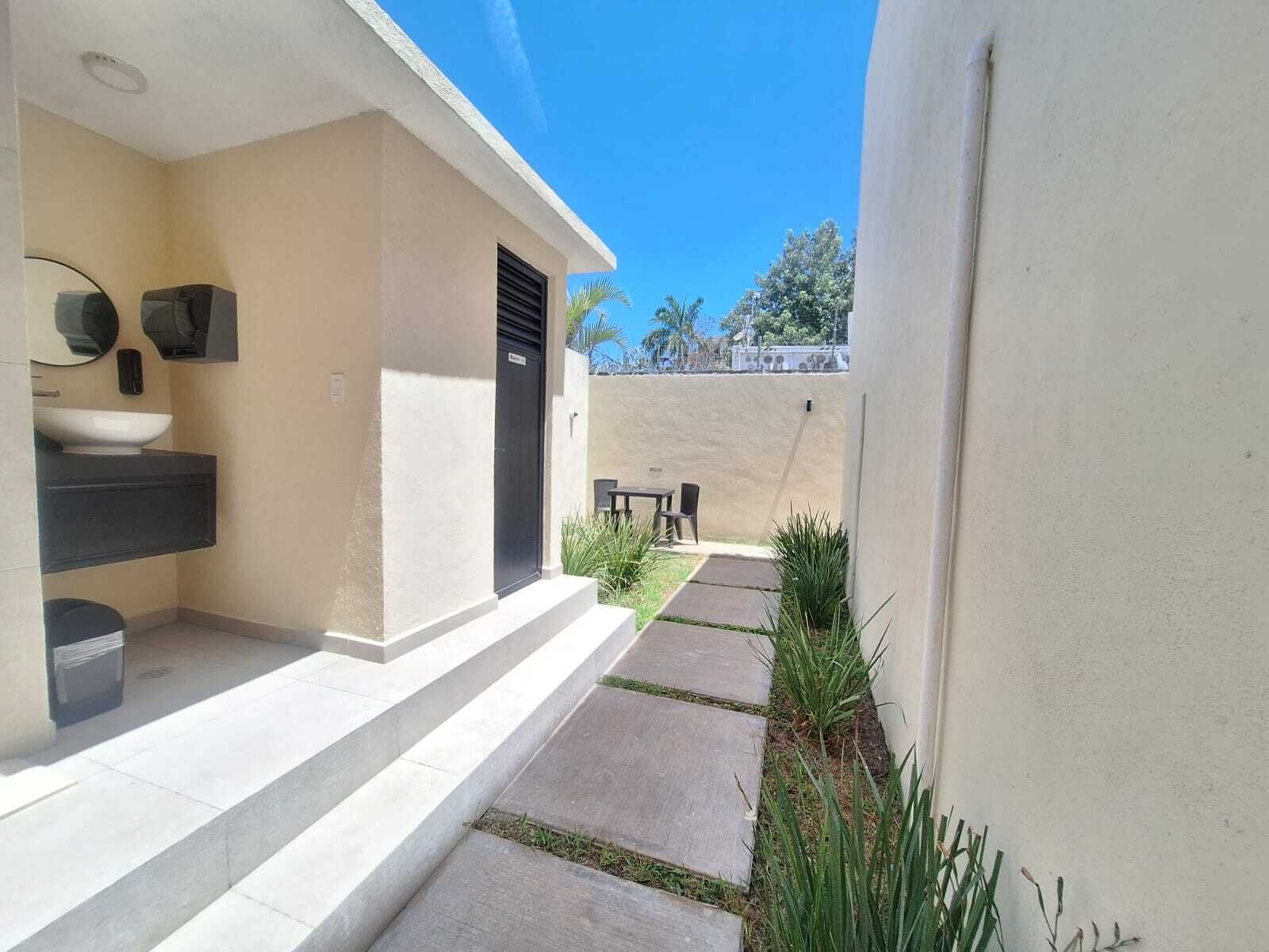 A modern outdoor area with a concrete pathway, a small table and chairs, and a wall-mounted sink.