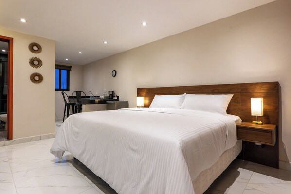 A hotel room with a large bed, wooden headboard, bedside lamps, a small desk with a chair, and a view of the outside through a window. - Hotel 28 (Cancun)