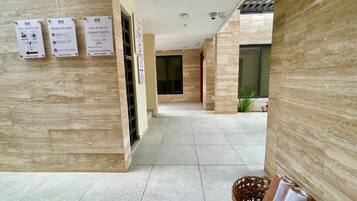 A hotel corridor with tiled flooring, a reception desk, and informational signs.