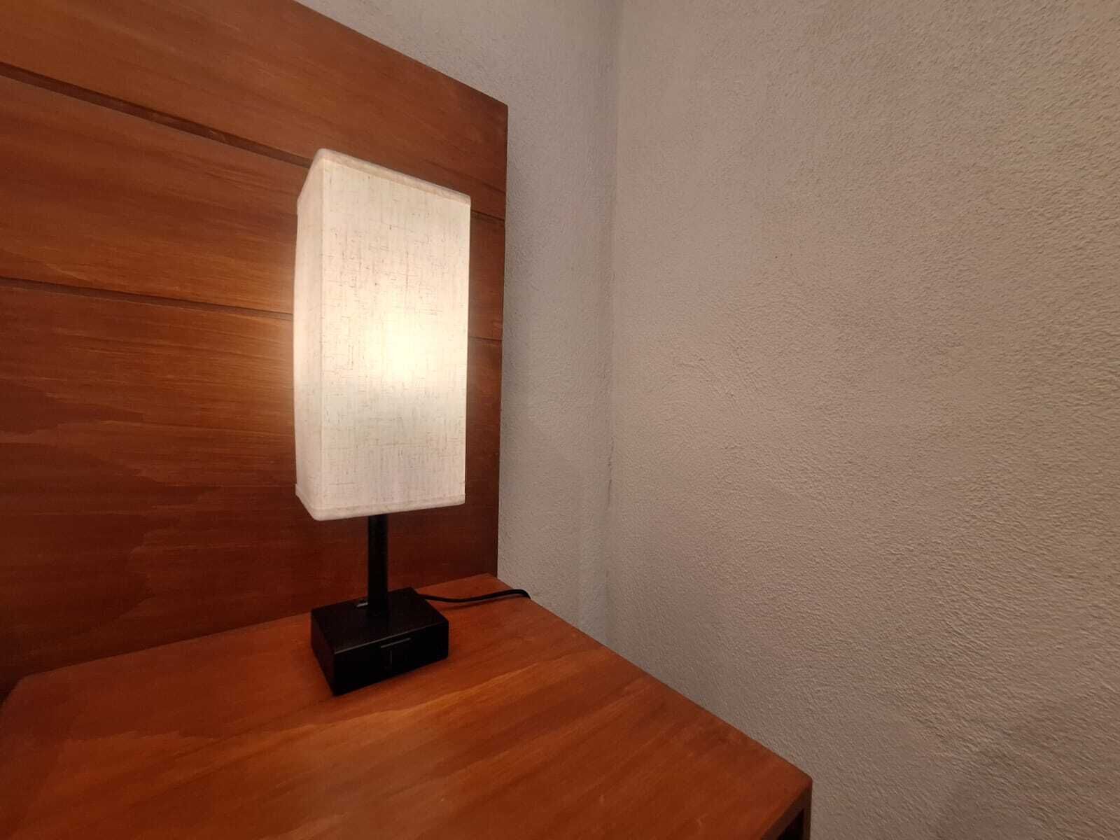 Una mesita de noche con una lámpara y un distribuidor de corriente.