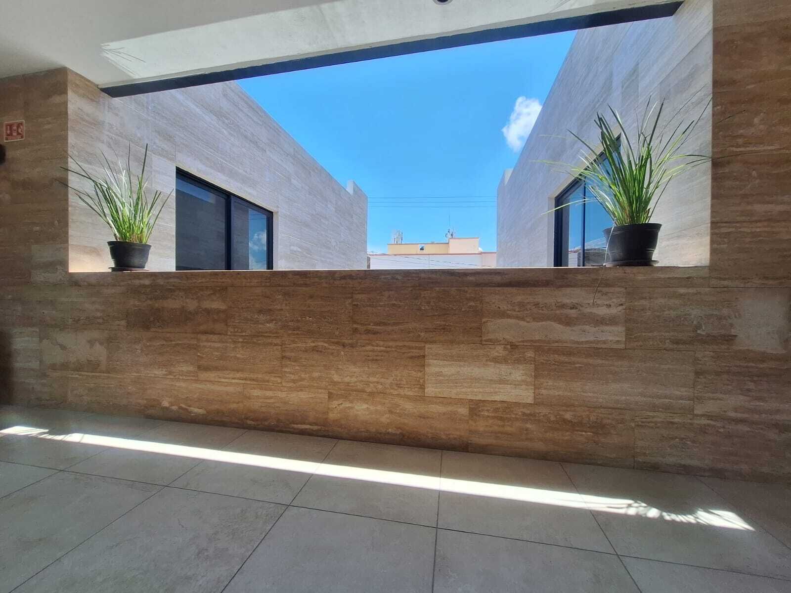 A modern interior with a view through a window, featuring a tiled floor and a wall with a geometric pattern.