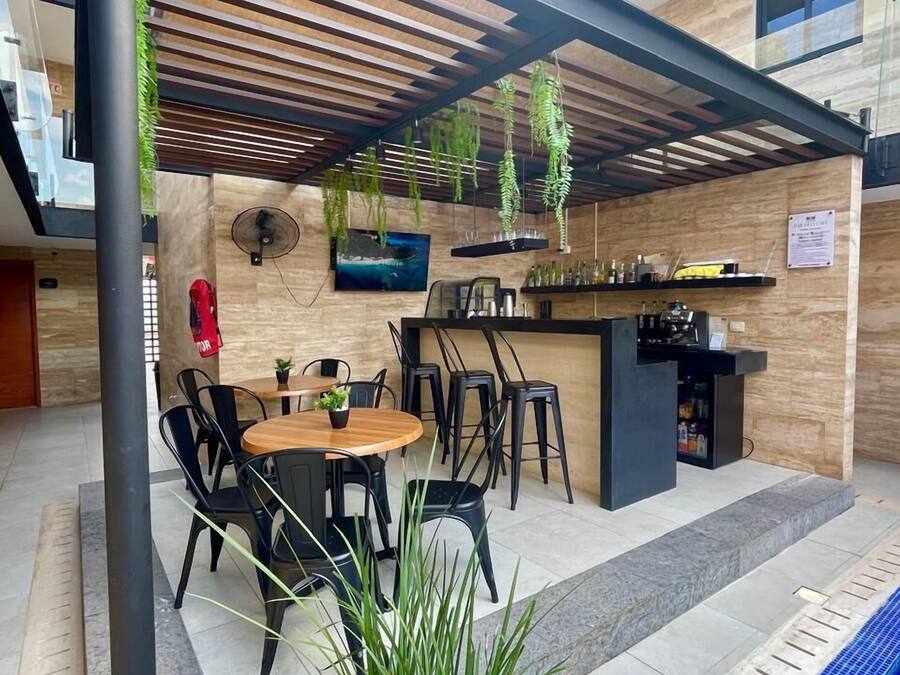 An outdoor patio area with a round wooden table and chairs, a bar counter, hanging plants, and a pool.