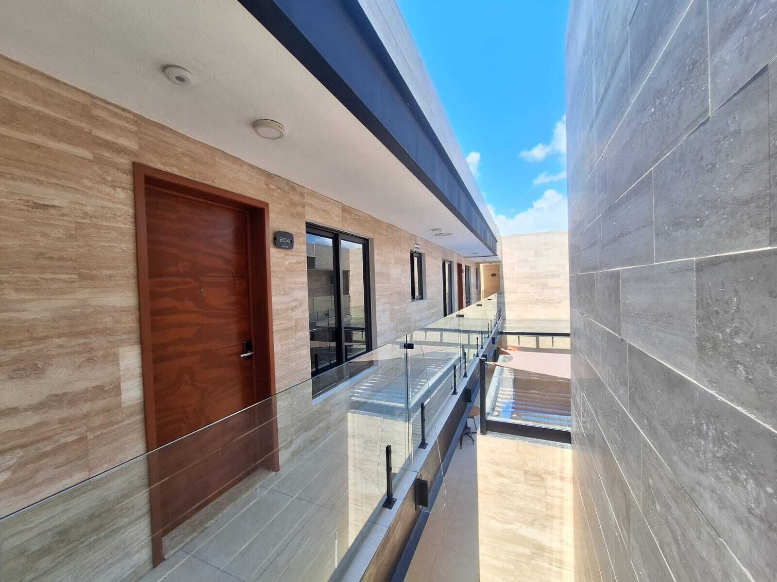 Un pasillo moderno de hotel con puerta de madera, barandillas de vidrio y suelo de baldosas.