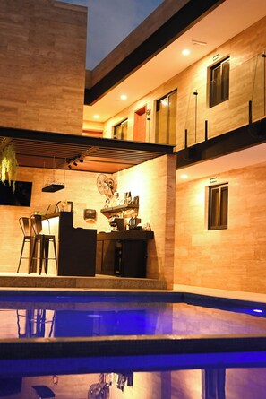 A modern multi-story building with a pool area, outdoor seating, and a bar. - Hotel 28 (Cancun)