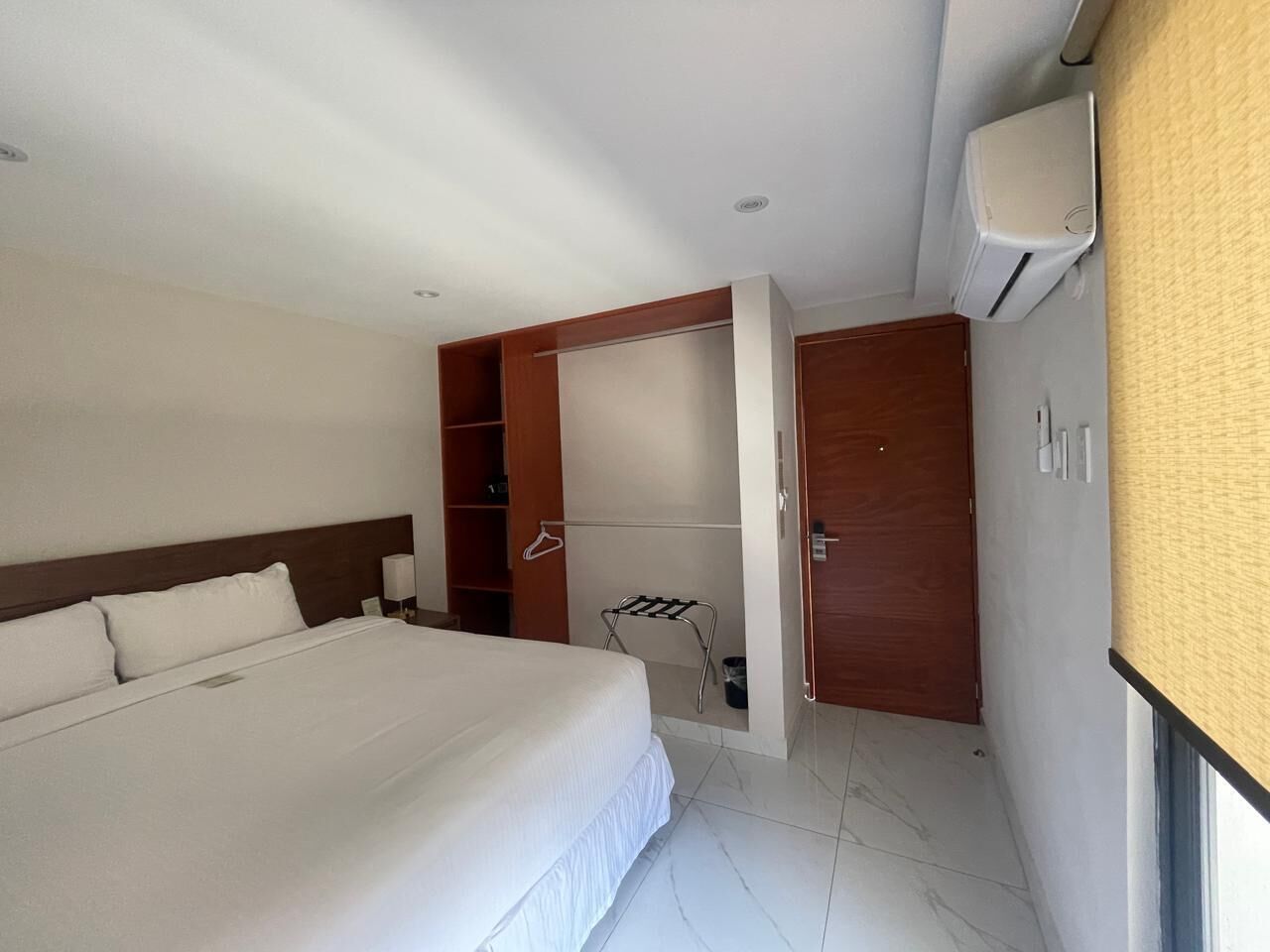 A hotel room with a large bed, a wardrobe, a drying rack, and a wall-mounted air conditioner.