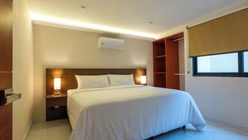 A hotel room with a bed, nightstands, a wall-mounted air conditioner, a window with a blind, and a wooden wardrobe.