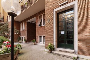 A courtyard with a brick building, potted plants, and a street lamp.
