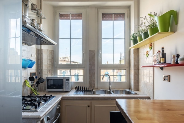 A kitchen with a gas stove, microwave, sink, and two windows.