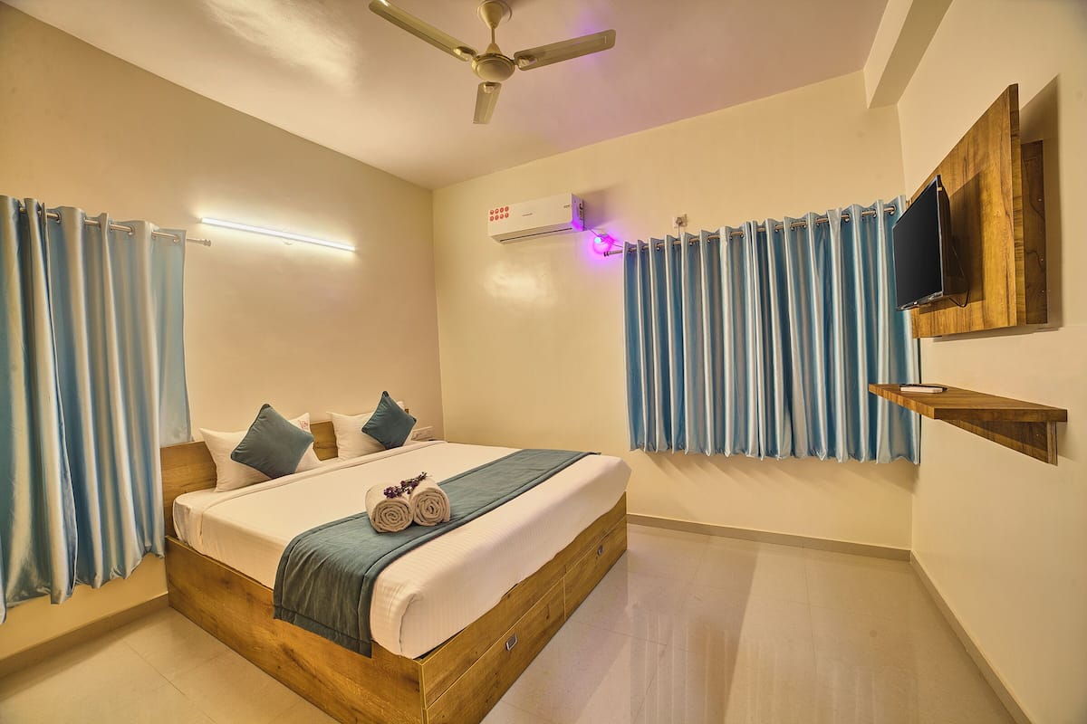 Une chambre moderne avec un lit en bois, un ventilateur de plafond, un appareil de climatisation et un téléviseur fixé au mur.