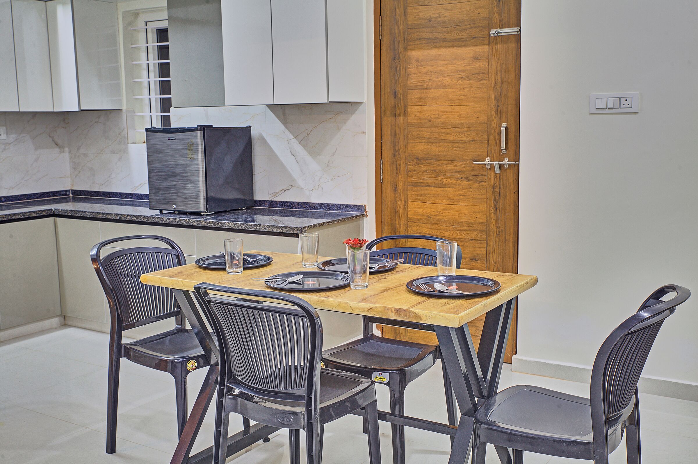 Un coin repas avec une table en bois et des chaises noires, une cuisine avec des meubles blancs et une porte en bois.