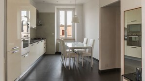 A modern kitchen with white cabinets, a dining table with chairs, and a window with a view. - GuestHost - Trastevere Station Bright Apartment with Terrace (Roma)