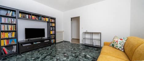 A living room with a flat-screen TV, bookshelves, a sofa, and a marble floor.