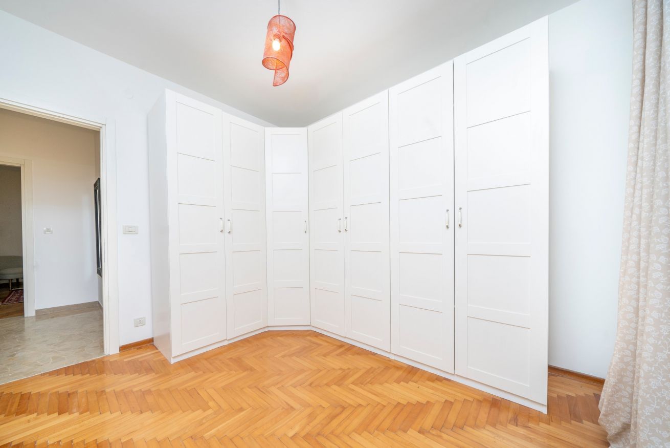 Una habitación con suelo de madera de diseño espiga, armarios blancos y una lámpara colgante.