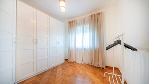 Une pièce avec un parquet en bois disposé en motif chevron, une armoire blanche et un étendoir.