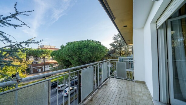 Un balcon donnant sur une route, des arbres et un bâtiment situé au loin.