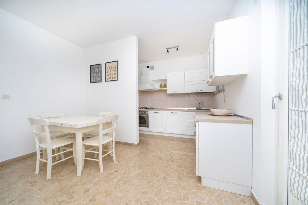 Een kleine keuken met witte kasten, een eettafel met stoelen en een kleine koelkast.
