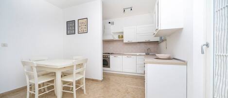 A compact kitchen with white cabinetry, a dining table with chairs, and a small refrigerator.