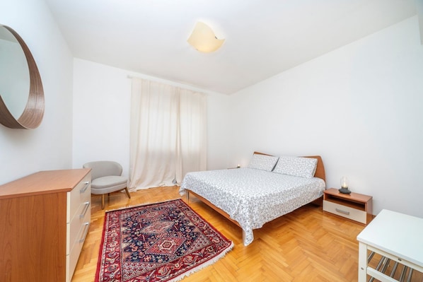 A bedroom with a bed, a desk, a chair, a rug, and a mirror.