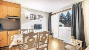 Ein kompakter Wohnbereich mit Küchenzeile, Essplatz und großem Fenster mit Vorhängen.