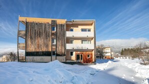 Ein modernes Gebäude mit Holzfassade und mehreren Balkonen, umgeben von Schnee.